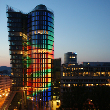 Ein Bild des bunt leuchtenden UNIQA Towers ein runder Turm mit Glasfassade