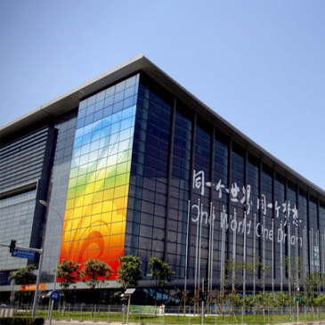 Das Bild zeigt das Chinese National Conference Center in Beijing ein quadratisches Gebäude mit Glasfassade und einem bunten Streifen