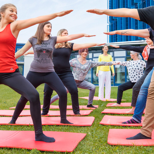Das Bild zeigt mehrere Personen bei Yogaübungen vor dem Aumüller Gebäude